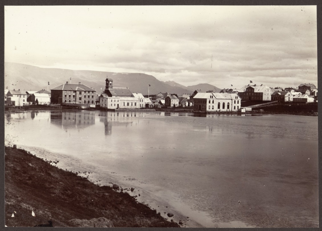 Reykjavík from the Tjörn [the Tarn, or Pond], ca. 1900. The view faces northeast and includes Parliament (center left), the national cathedral to its right and Menntaskólinn í Reykjavík, the country’s main high school at the time (to the right, with flag flying). The mountain Esja rises in the background. From the Icelandic and Faroese Photographs of Frederick W.W. Howell.